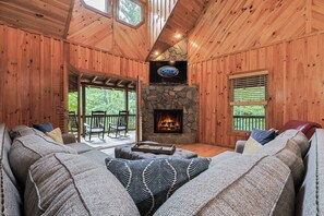 A cozy cabin interior with a stone fireplace, wooden walls, and a large sectional sofa. - Where The Mountains Meet | Blue Ridge, GA (Epworth)