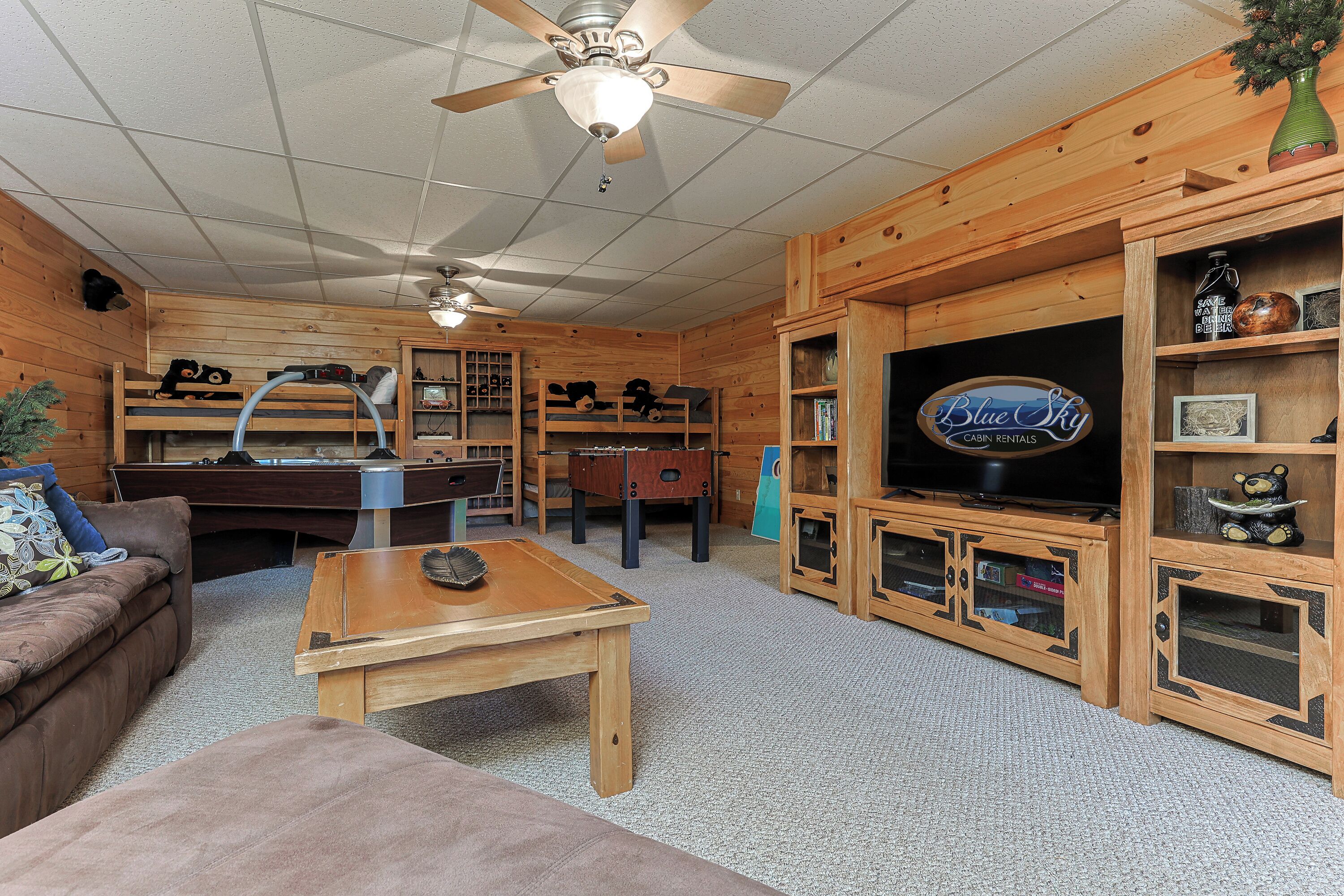 A room with a pool table, a sofa, a coffee table, a ceiling fan, and wooden shelving with a television.