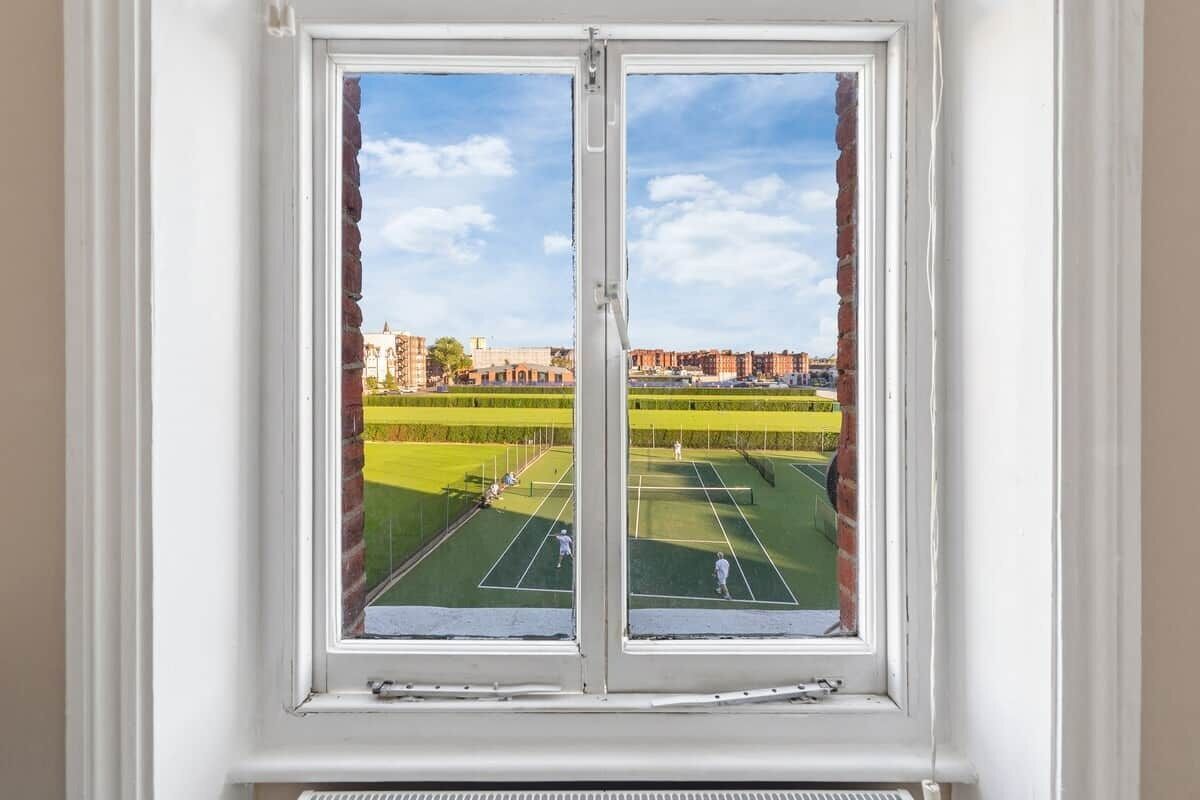 A window with a view of a tennis court and surrounding buildings.
