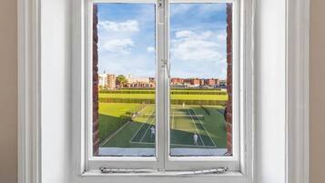 A window with a view of a tennis court and surrounding buildings.