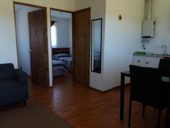A room with a bed, a desk, a chair, a mirror, and a door leading to another room.