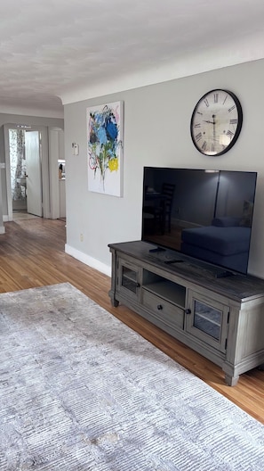 Un soggiorno con televisione, un orologio e un quadro astratto colorato appeso al muro.