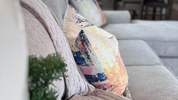 Una sala moderna con un sofá gris, almohadones coloridos, una pequeña planta en maceta e iluminación colgante.