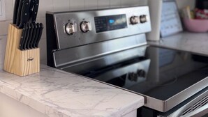 Una cocina con estufa de acero inoxidable, armarios blancos y encimera de mármol.