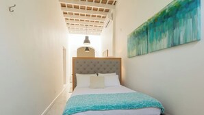 A bedroom with a bed, a headboard, a painting on the wall, and a ceiling with wooden beams. - 152 Sol by Stay with Bear (San Juan)