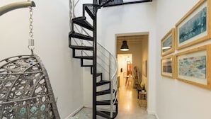 A spiral staircase with a metal railing, a wicker chair, and framed artwork on the walls. - 152 Sol by Stay with Bear (San Juan)
