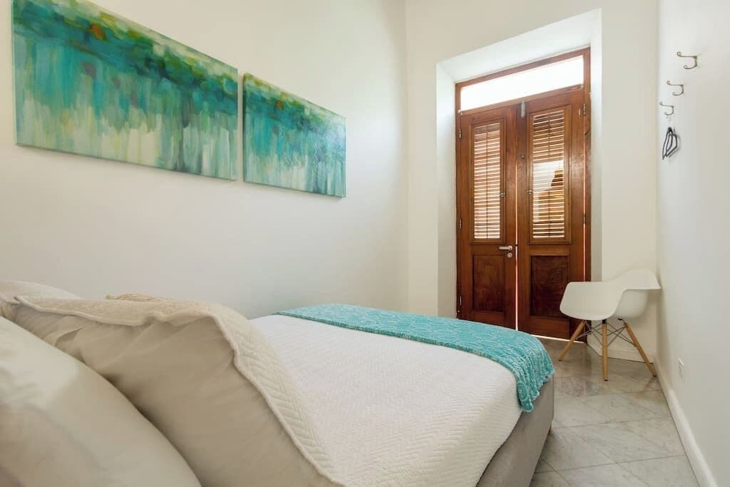 A bedroom with a bed, a chair, and two paintings on the wall.