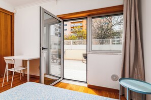A room with a sliding glass door leading to an outdoor balcony, a white table with a chair, and a small blue table. - Lisbon Easy Stay (Lisbon)