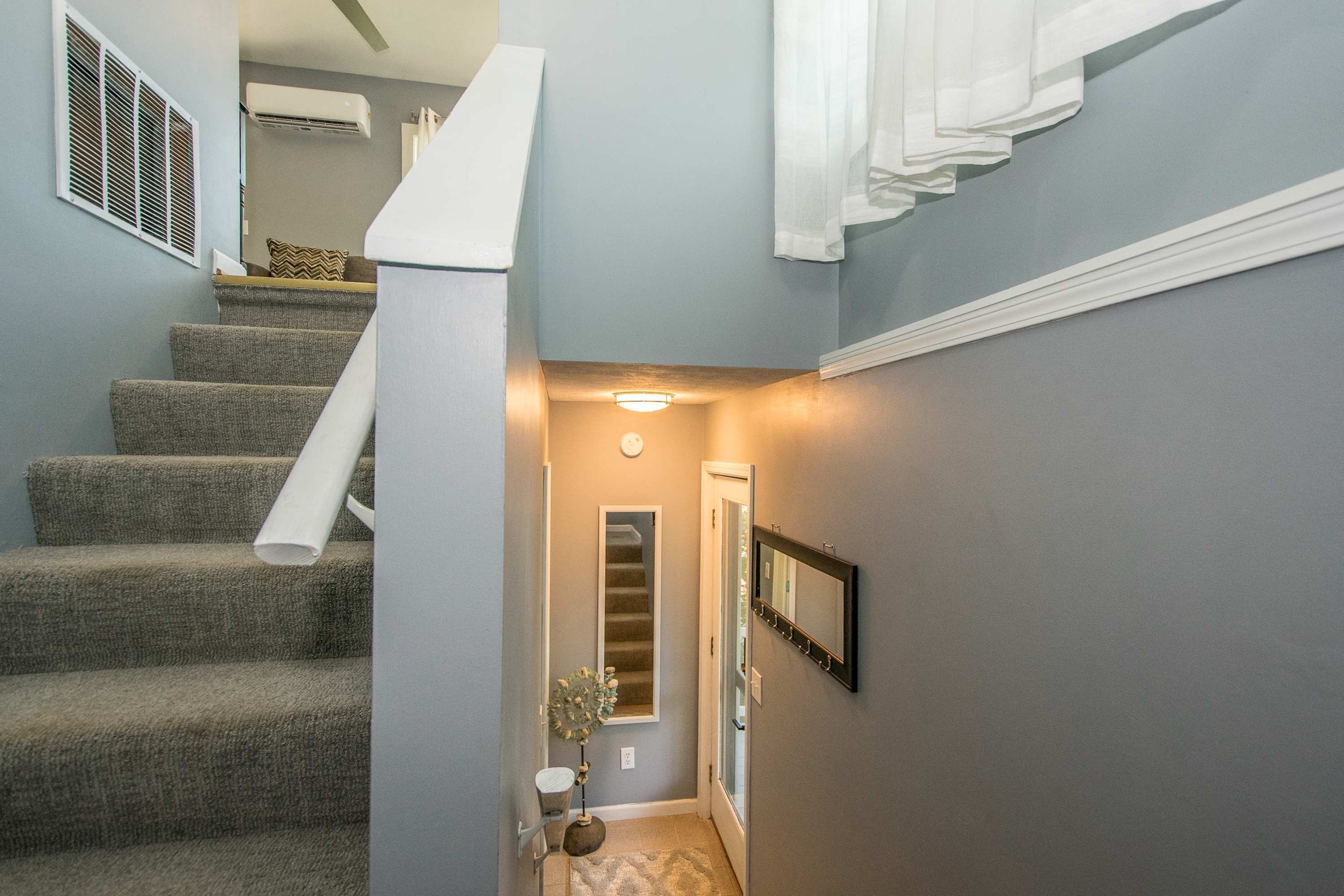 A staircase with carpeted steps, a wall-mounted air conditioner, a small plant, and a door leading to another room.