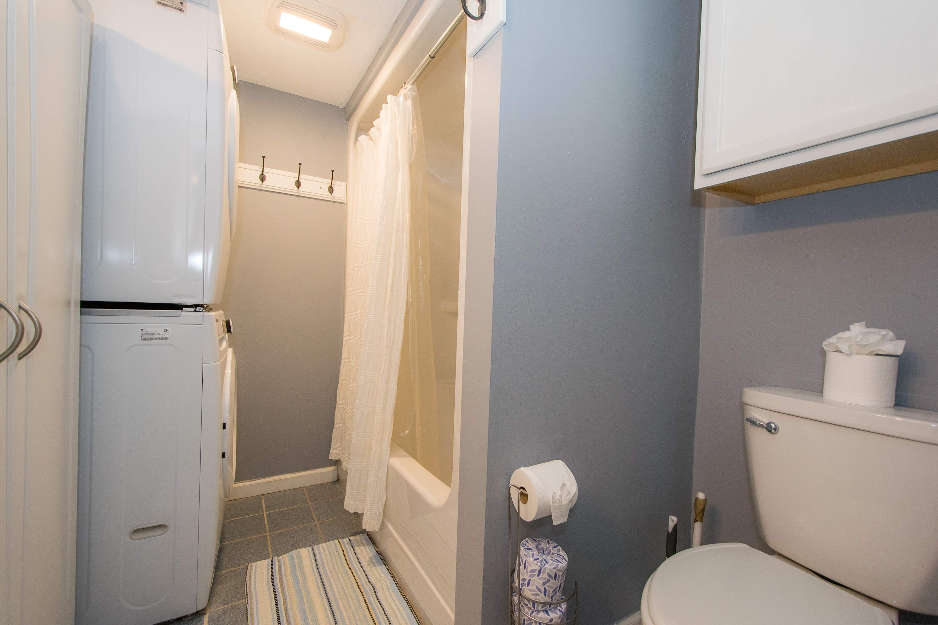 Et badeværelse med toilet, bruser med gardin, vaskemaskine og håndklædestige.