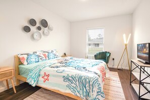 Ein Schlafzimmer mit Bett, Nachttisch, Stuhl, Fernseher und einem Fenster mit Jalousien.