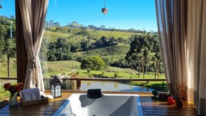 Une terrasse en bois avec un jacuzzi, des rideaux et une vue sur un paysage verdoyant.
