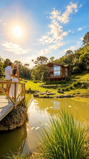 Eine Holzhütte mit einer Terrasse, die auf einen Teich mit üppiger Vegetation und Bäumen blickt.
