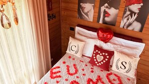 Une chambre confortable avec un lit agrémenté d’une décoration en forme de cœur sur laquelle on peut lire les mots « TE AMO », un lustre et des tableaux encadrés accrochés au mur.