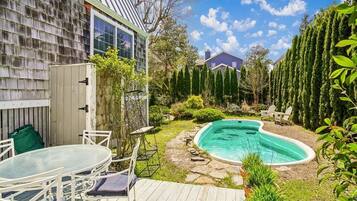 A backyard with a swimming pool, a deck with outdoor furniture, and a house with a shingled exterior.