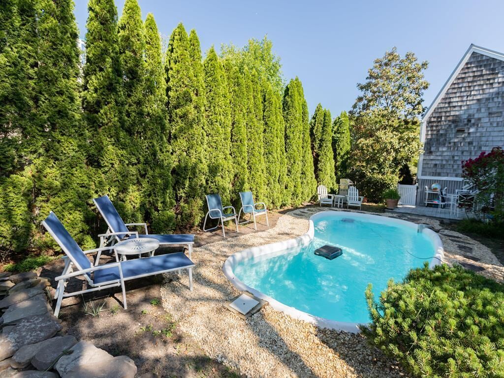 A swimming pool with lounge chairs, surrounded by trees and a building.