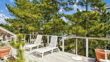 A wooden deck with white lounge chairs and potted plants.