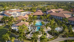 A resort with multiple buildings, a central swimming pool, and surrounding palm trees. - PGA National Cottage | Pool, Spa & PGA Golf (Palm Beach Gardens)