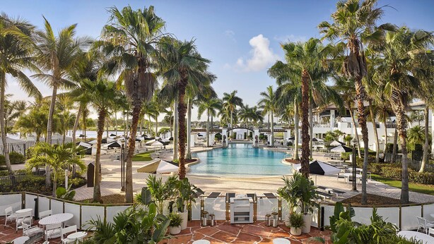 A resort pool area with palm trees, lounge chairs, and umbrellas. - PGA National Cottage | Pool, Spa & PGA Golf (Palm Beach Gardens)