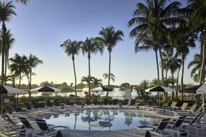 A pool area with lounge chairs, umbrellas, and palm trees.