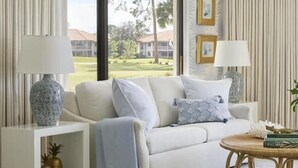 A living room with a sofa, two lamps, a coffee table, and a view of a golf course. - PGA National Cottage | Pool, Spa & PGA Golf (Palm Beach Gardens)