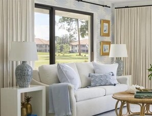 A living room with a sofa, two lamps, a coffee table, and a view of a golf course.