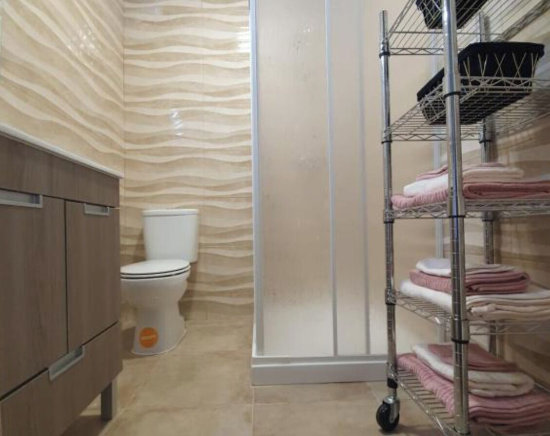 Een badkamer met toilet, wastafel en een metalen plank met opgevouwen handdoeken.