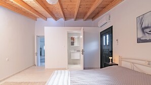 A bedroom with a bed, a nightstand, a door, and a hallway leading to a bathroom. - Villa Taxiarchis by Corfuescapes  (Corfu)