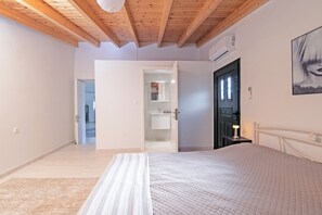 A bedroom with a bed, a nightstand, a door, and a hallway leading to a bathroom. - Villa Taxiarchis by Corfuescapes  (Corfu)
