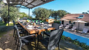 An outdoor dining area with a covered table, chairs, and a poolside setting. - Villa Taxiarchis by Corfuescapes  (Corfu)