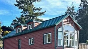 A two-story wooden cabin with a green roof, a large window on the upper floor, and a deck. - Rogue River Landing Resort (Gold Beach)