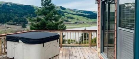 Une terrasse en bois avec un jacuzzi, offrant une vue sur un paysage vallonné.