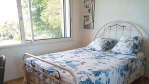 A single bed with a metal frame, a window with a view of trees, and a wall-mounted picture. - Apartment ❤️ quiet and air-conditioned, sea on foot in 7 min! (carqueiranne)