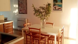 A dining area with a white table, wooden chairs, a vase with plants, a wall-mounted air conditioner, and a poster. - Apartment ❤️ quiet and air-conditioned, sea on foot in 7 min! (carqueiranne)