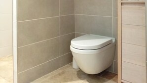 A corner bathroom with a toilet, tiled walls, and a wooden cabinet. - Apartment ❤️ quiet and air-conditioned, sea on foot in 7 min! (carqueiranne)