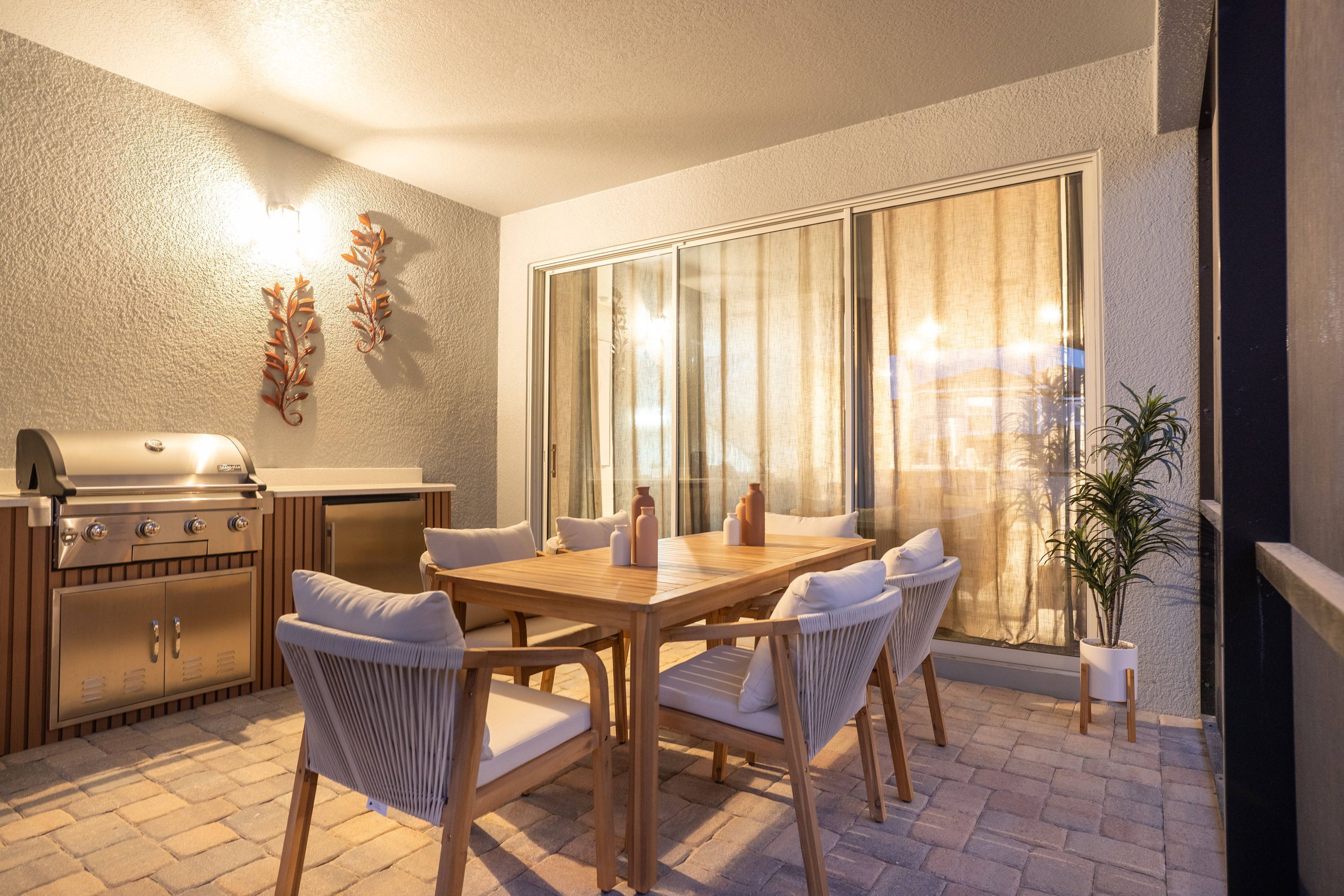 Une terrasse extérieure avec une table et des chaises en bois, un barbecue et une plante en pot.