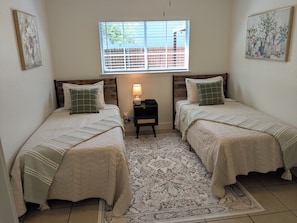 A bedroom with two beds, a nightstand, a lamp, and a window with blinds. - Cozy Seguin 3BR/Family & Travel friendly (Seguin)