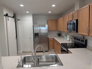 Una cocina moderna con electrodomésticos de acero inoxidable, armarios de madera, microondas integrado y dispensador de agua.