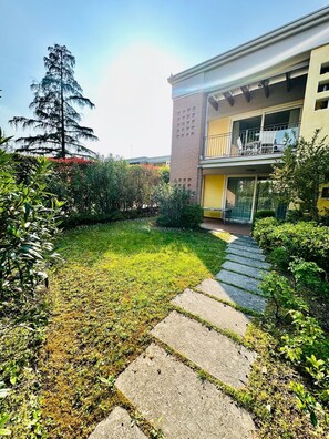 Ein Wohngebäude mit Balkon, einem steinernen Weg zum Eingang und einem gepflegten Rasen.