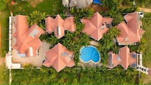 Ein Resort mit mehreren Gebäuden, einem zentral gelegenen Schwimmbad und umliegenden Palmen.