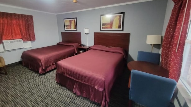 A hotel room with two beds, a desk, a chair, a lamp, and a window with curtains.