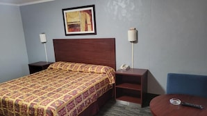 A hotel room with a bed, bedside tables, a desk with a phone, a chair, and a round table with a remote control.