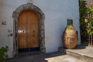 A wooden door with a metal arch, a large terracotta pot, and a small window on a white wall. - M'incanto Holiday home (Campania)