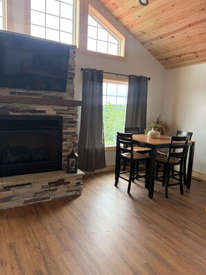 A dining area with a stone fireplace, wooden ceiling, and large windows.