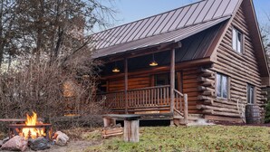 A log cabin with a porch, a fire pit, and a metal roof.