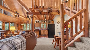 A log cabin interior with a living room, kitchen, and staircase.