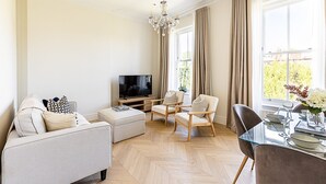 A modern living room with a flat-screen TV, a sofa, two armchairs, a glass dining table, and a chandelier. - Bright & Modern Hampstead Apartment (London)
