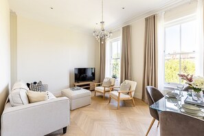 A modern living room with a flat-screen TV, a sofa, two armchairs, a glass dining table, and a chandelier. - Bright & Modern Hampstead Apartment (London)