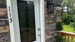 A house with a stone exterior, a white door with a number '113' on it, a welcome mat, and a potted plant with flowers. - Private Oasis Awaits ! Hot Tub, Fire Pit, nap in the Hammock under the trees (Canadensis)