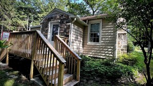 A two-story cabin with a wooden staircase, a stone exterior, and a small porch. - Private Oasis Awaits ! Hot Tub, Fire Pit, nap in the Hammock under the trees (Canadensis)